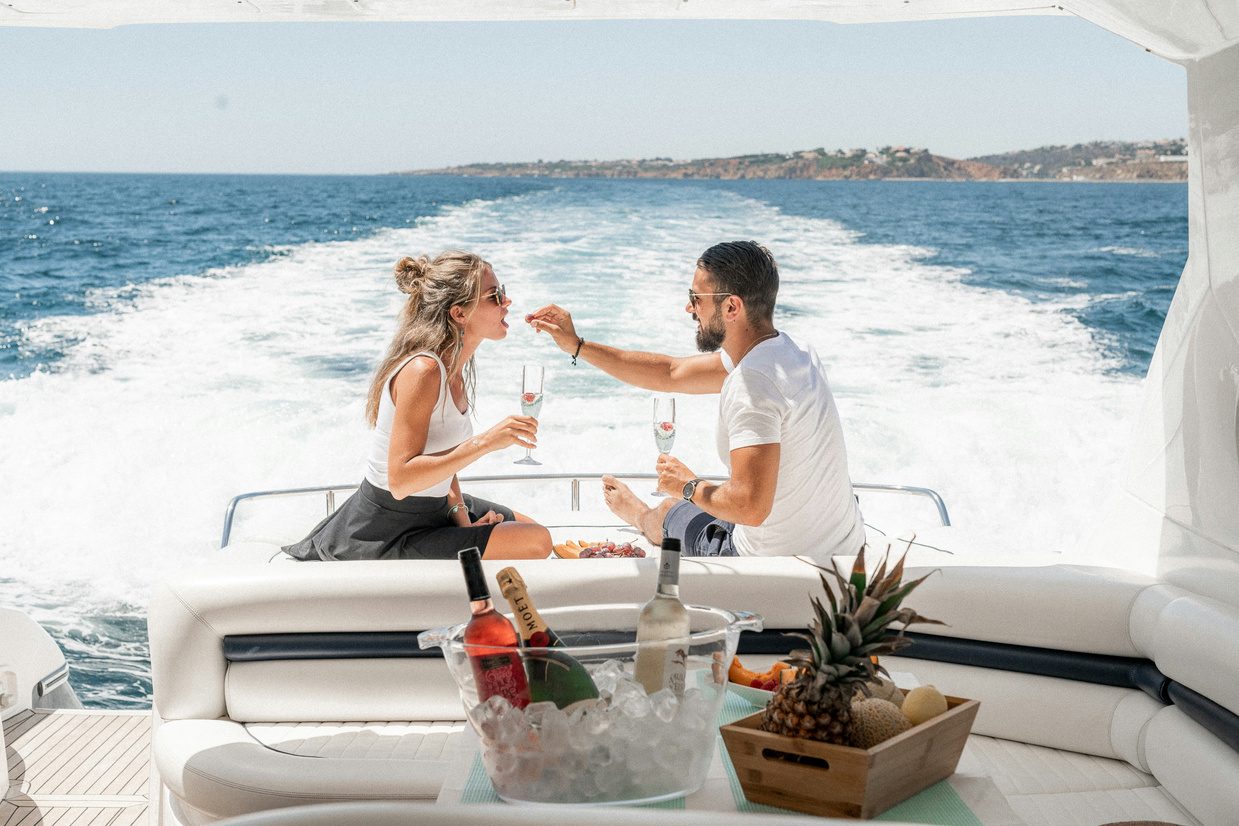 Two guests sharing champagne and fruit on the aft deck of a motor yacht under way, the wake calm behind them