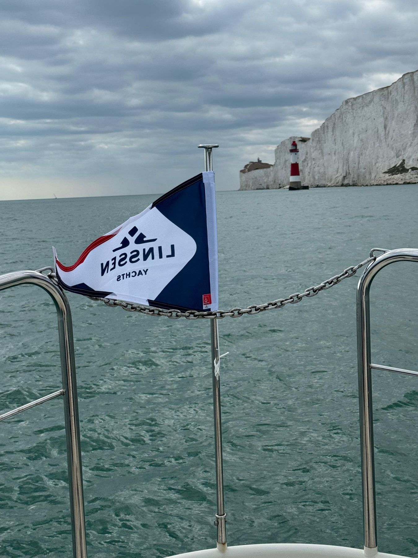 A burgee at the stern rail, with a lighthouse and chalk cliffs across the water