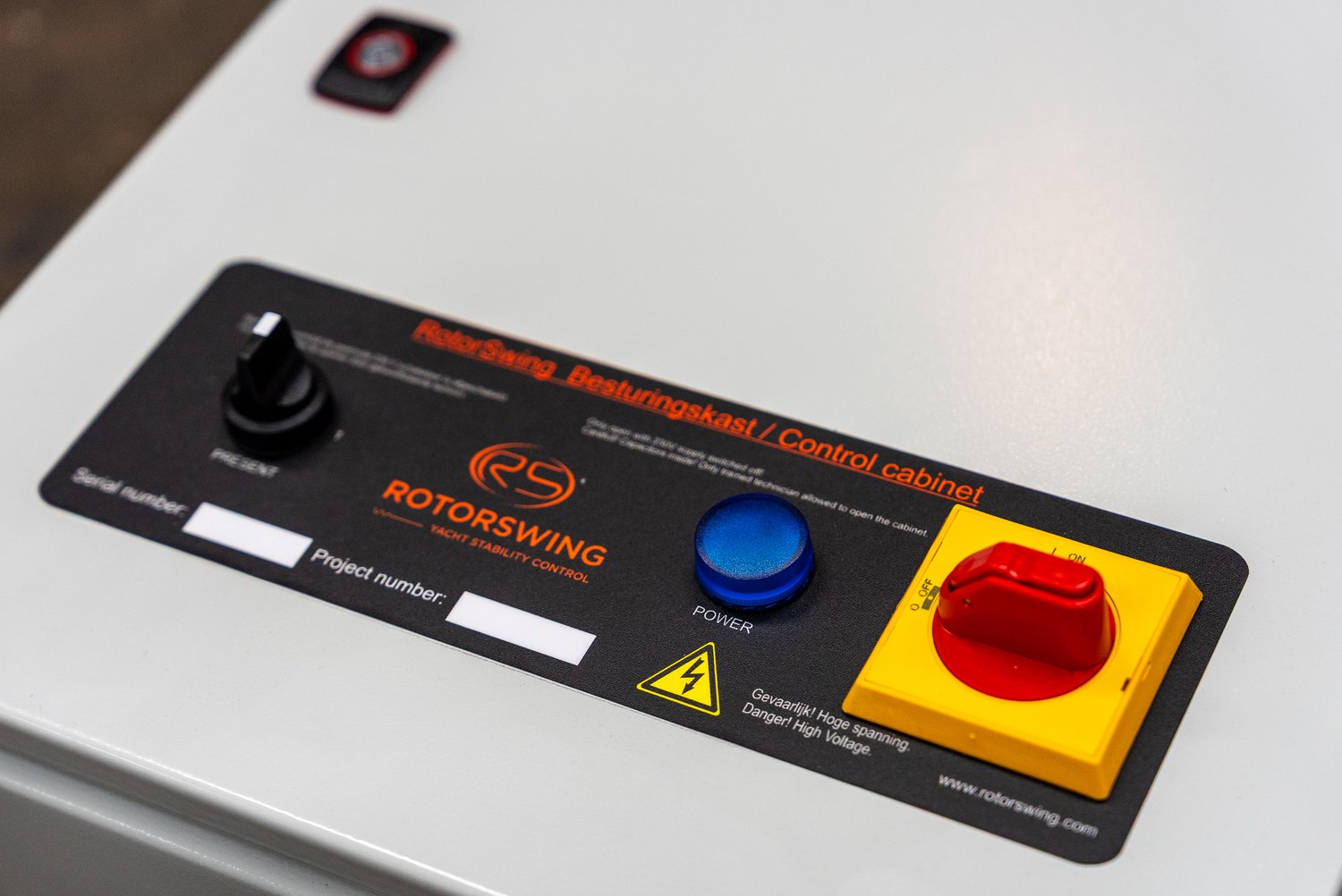 The control cabinet front plate at an angle: a black label with orange RotorSwing lettering, a selector knob, a blue power lamp and a red isolator switch in a yellow housing