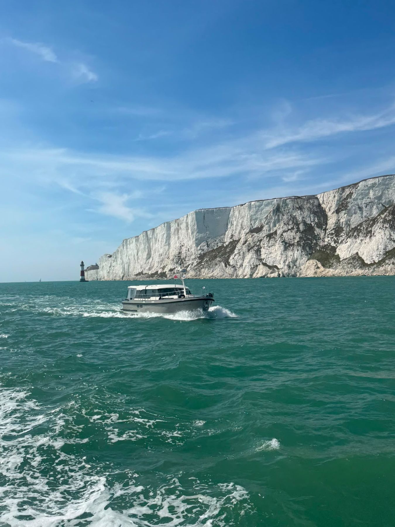 A motor yacht under way in turquoise water below white chalk cliffs