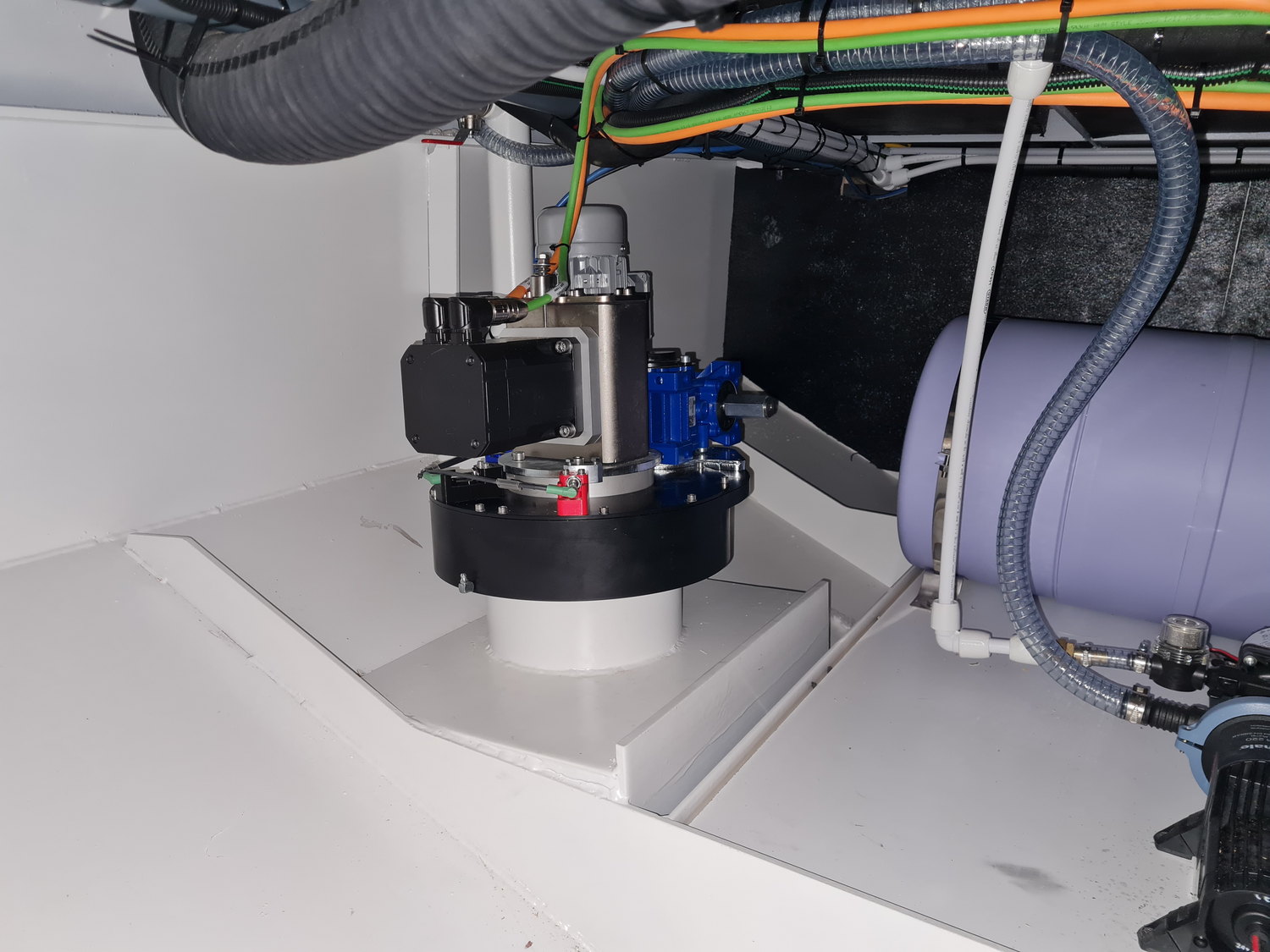 An installed RotorSwing drive unit in a yacht technical compartment, bolted to its white mounting platform under cable trays and pipework