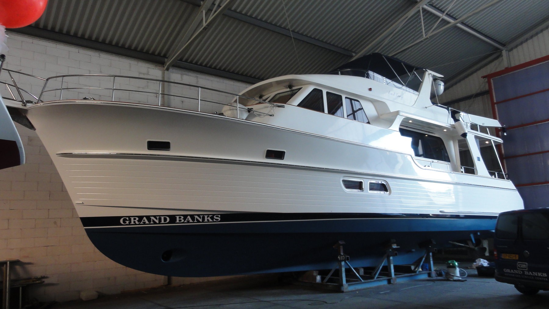 A white motor yacht with a dark blue hull standing on keel blocks and stands inside a covered yard shed, hauled out for work