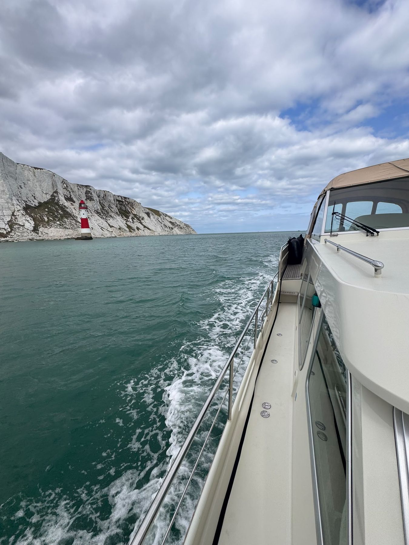 The side deck of a motor yacht under way, her wake running aft and chalk cliffs beyond