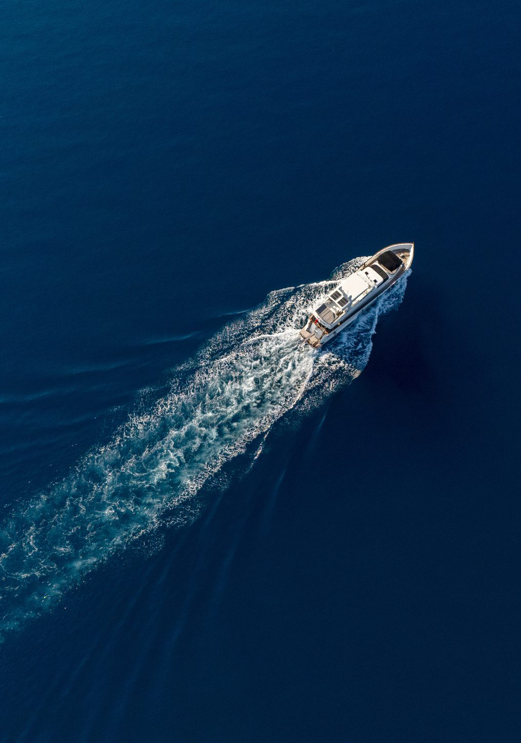 A motor yacht under way on deep blue open water, seen from directly above, its wake trailing behind