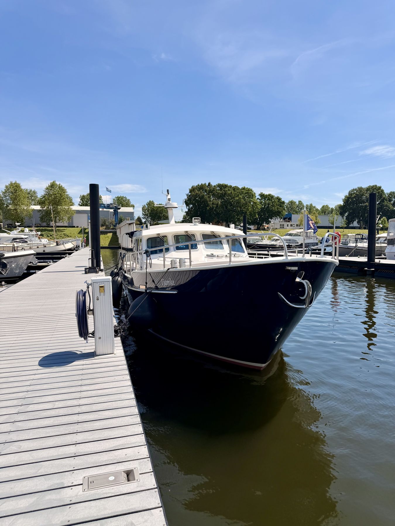 A dark blue motor yacht lying alongside a pontoon on a clear day
