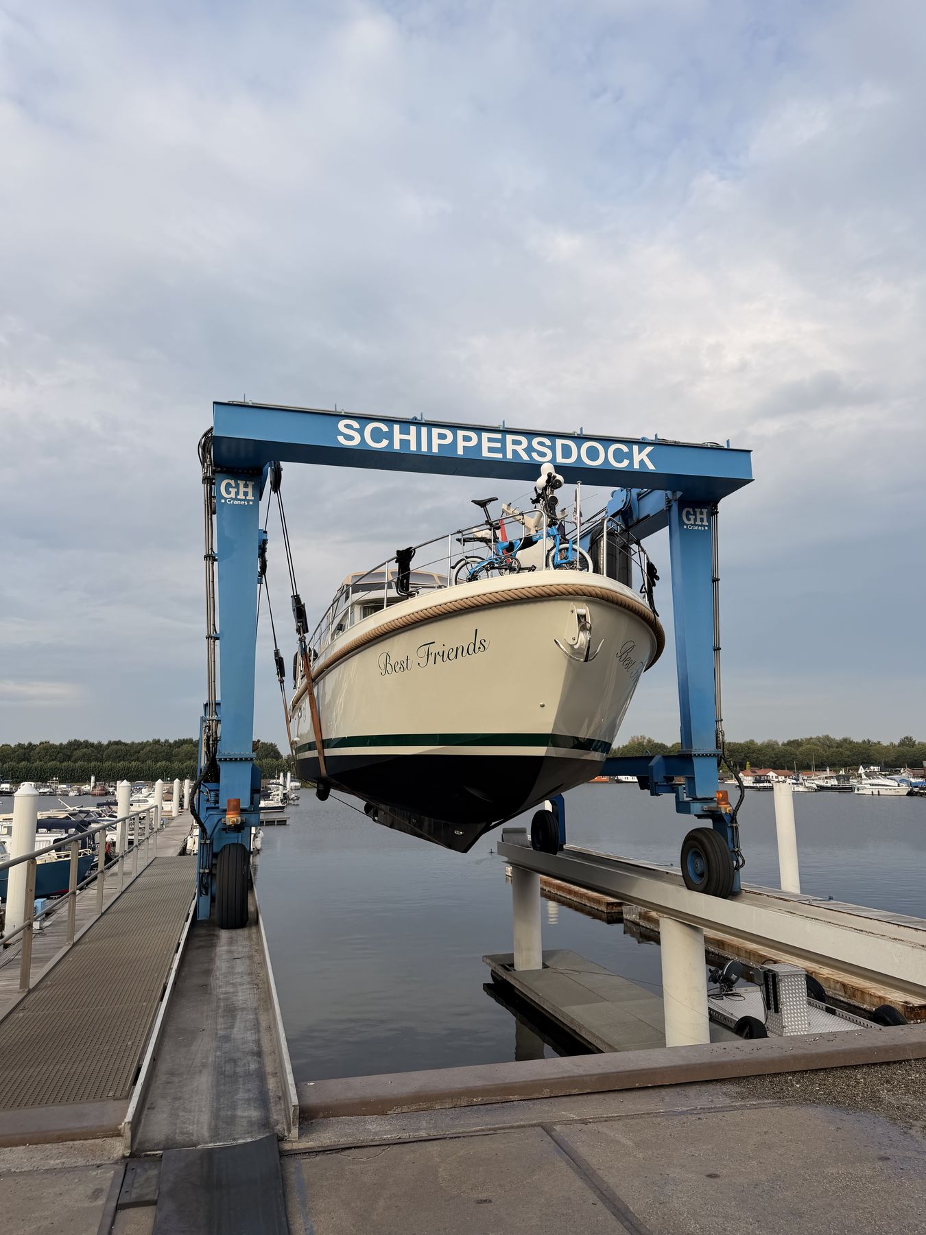 A motor yacht lifted clear of the water in a yard hoist, the marina behind her