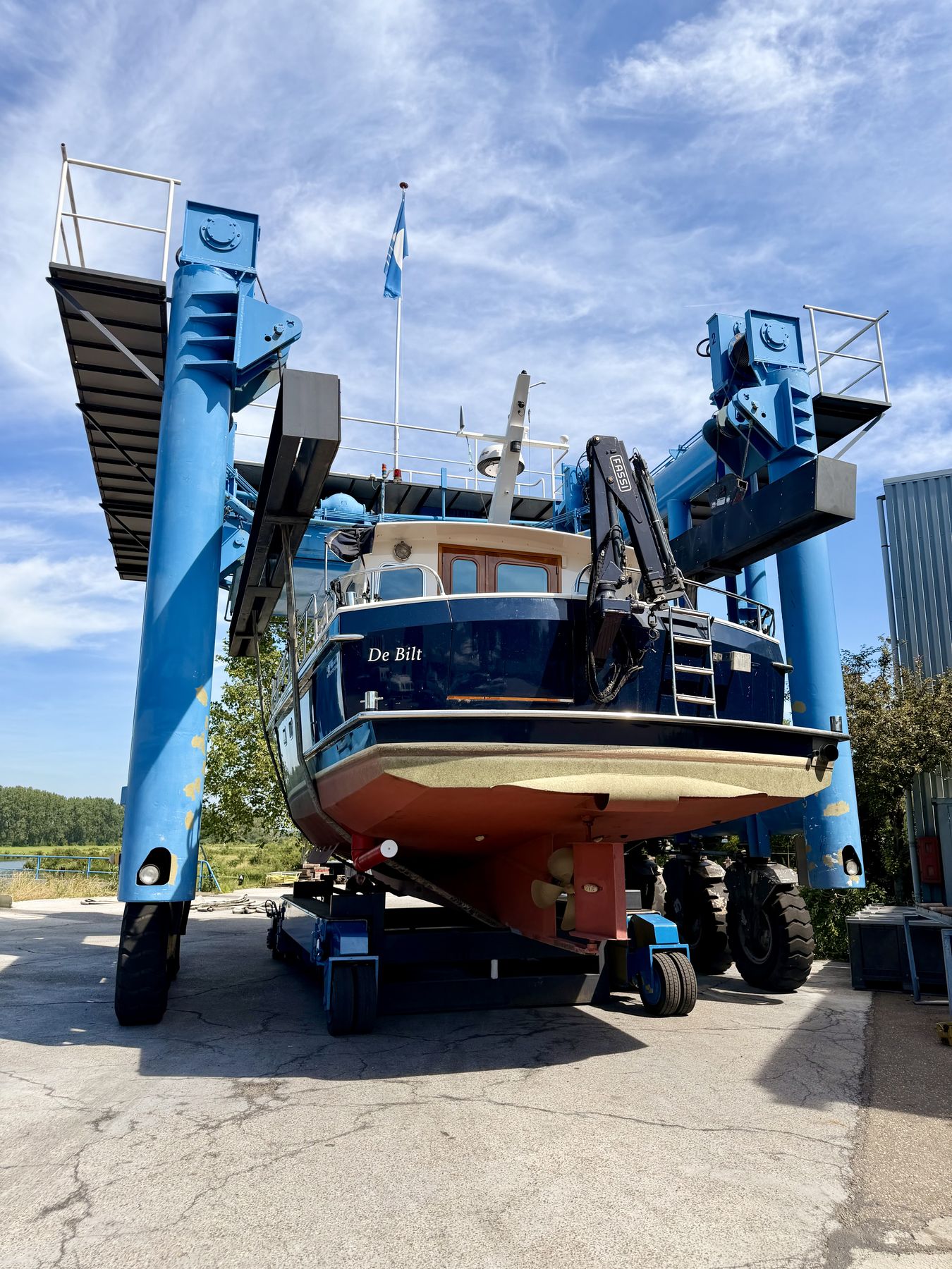 A motor yacht in the slings of a blue travel lift at the yard, hauled out for work